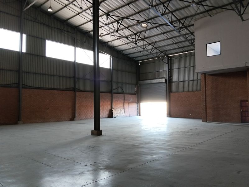 Spacious industrial warehouse featuring high ceilings, exposed brickwork, concrete flooring, and a large roller shutter door for efficient access.