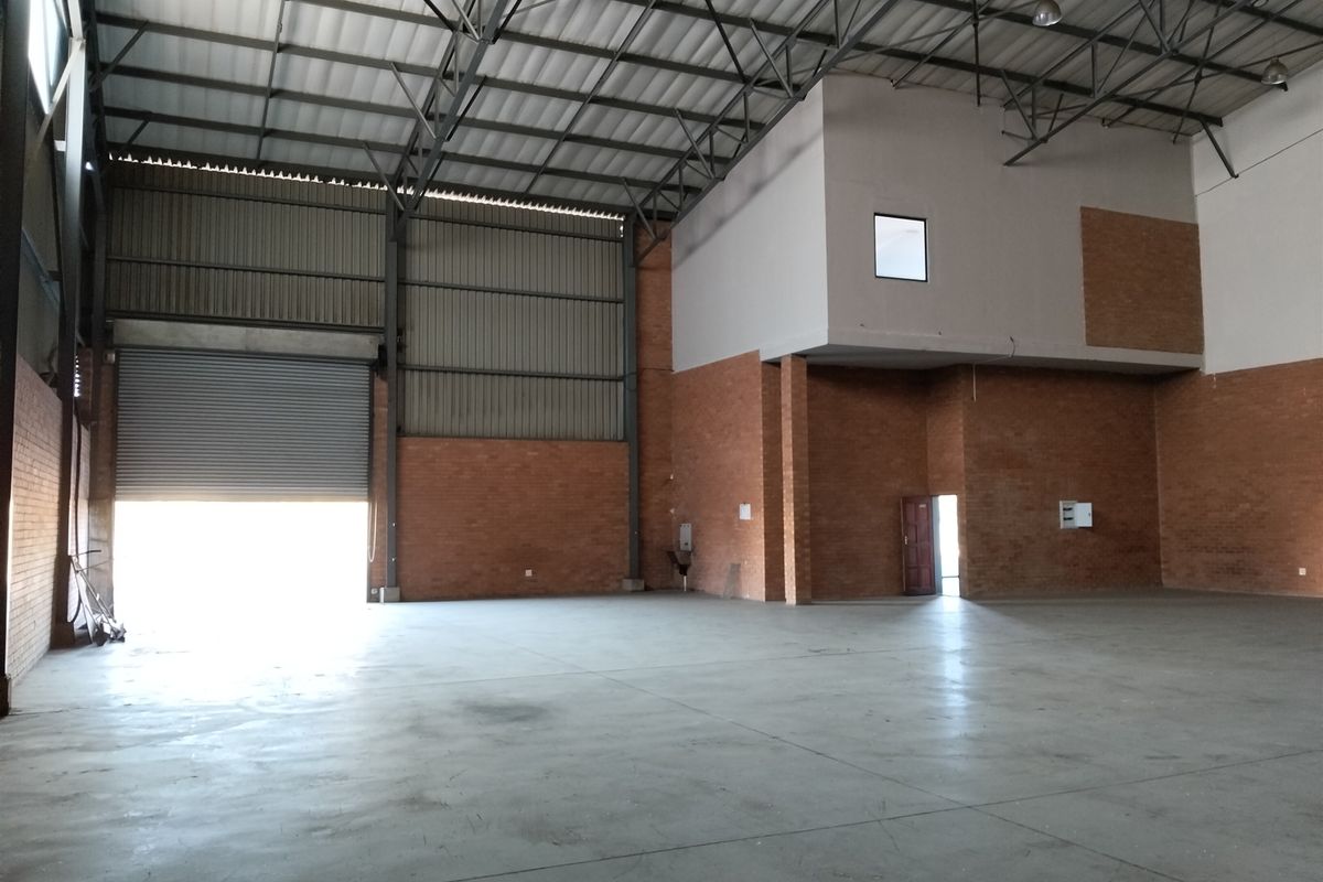 Spacious industrial warehouse unit featuring high ceilings with exposed steel trusses, concrete flooring, exposed brick walls, and a large roller shutter door.