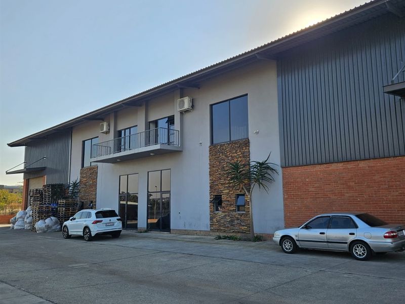 Front elevation of an industrial warehouse building featuring a combination of metal cladding, brickwork, stone accents, and an upper-level balcony.