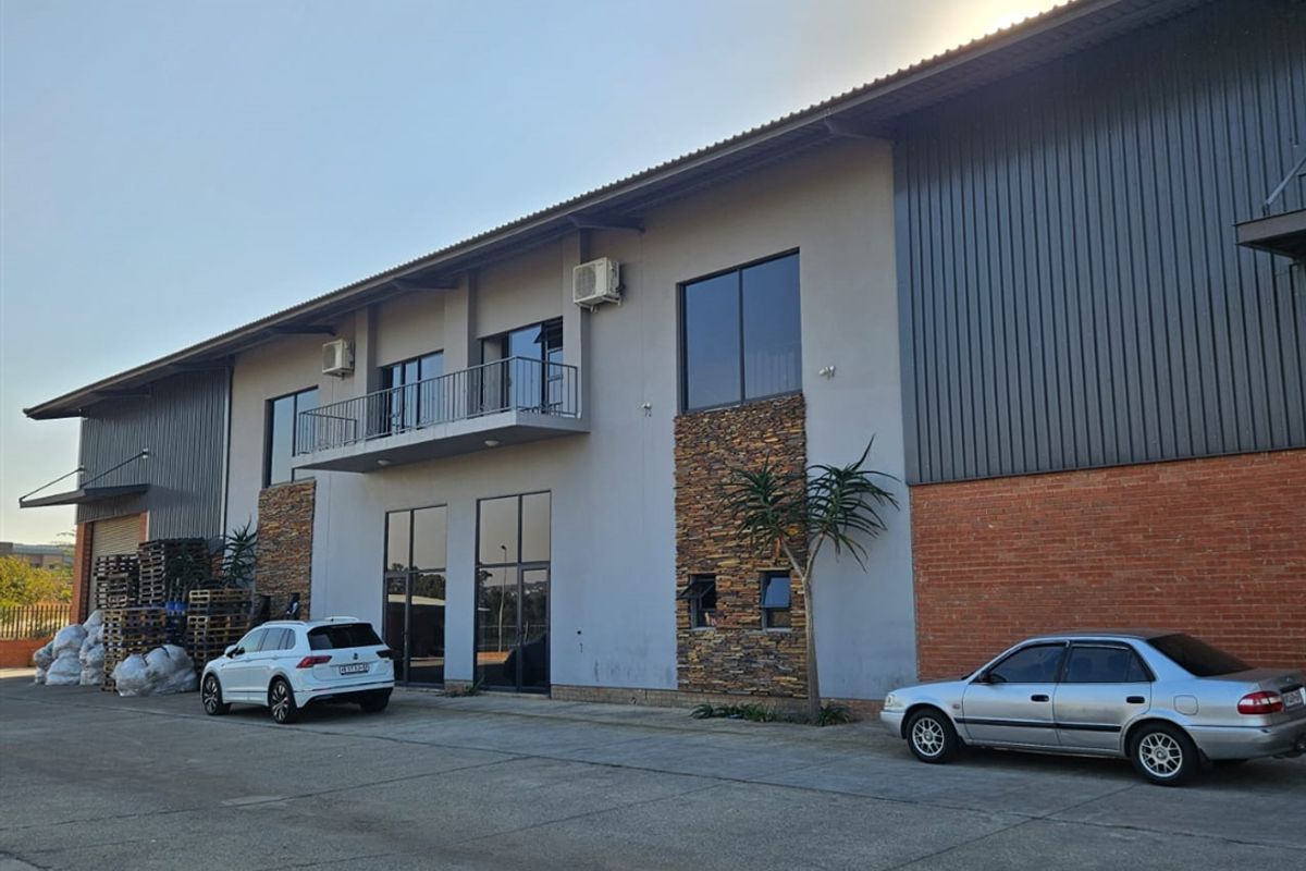 Front elevation of an industrial warehouse building featuring a combination of metal cladding, brickwork, stone accents, and an upper-level balcony.