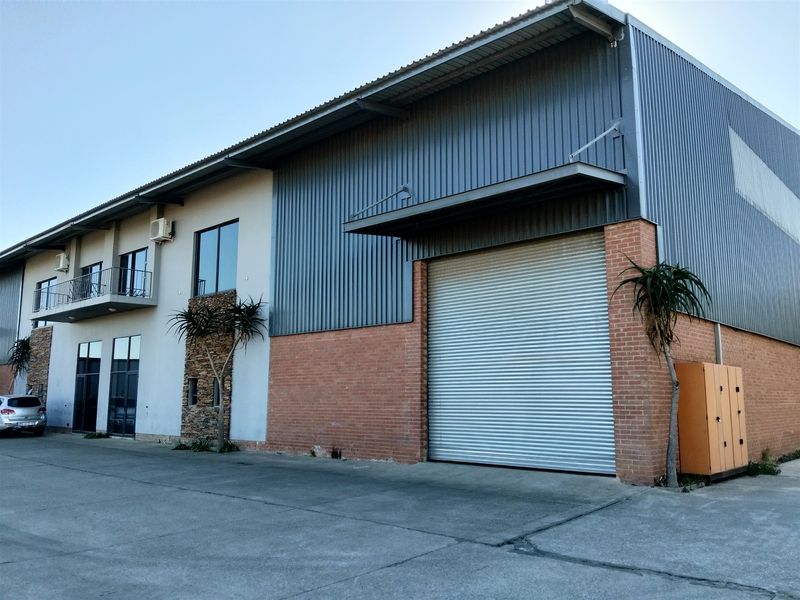 Industrial property featuring a large roller shutter door, metal and brick facade, and an upper-level balcony with concrete driveway access.