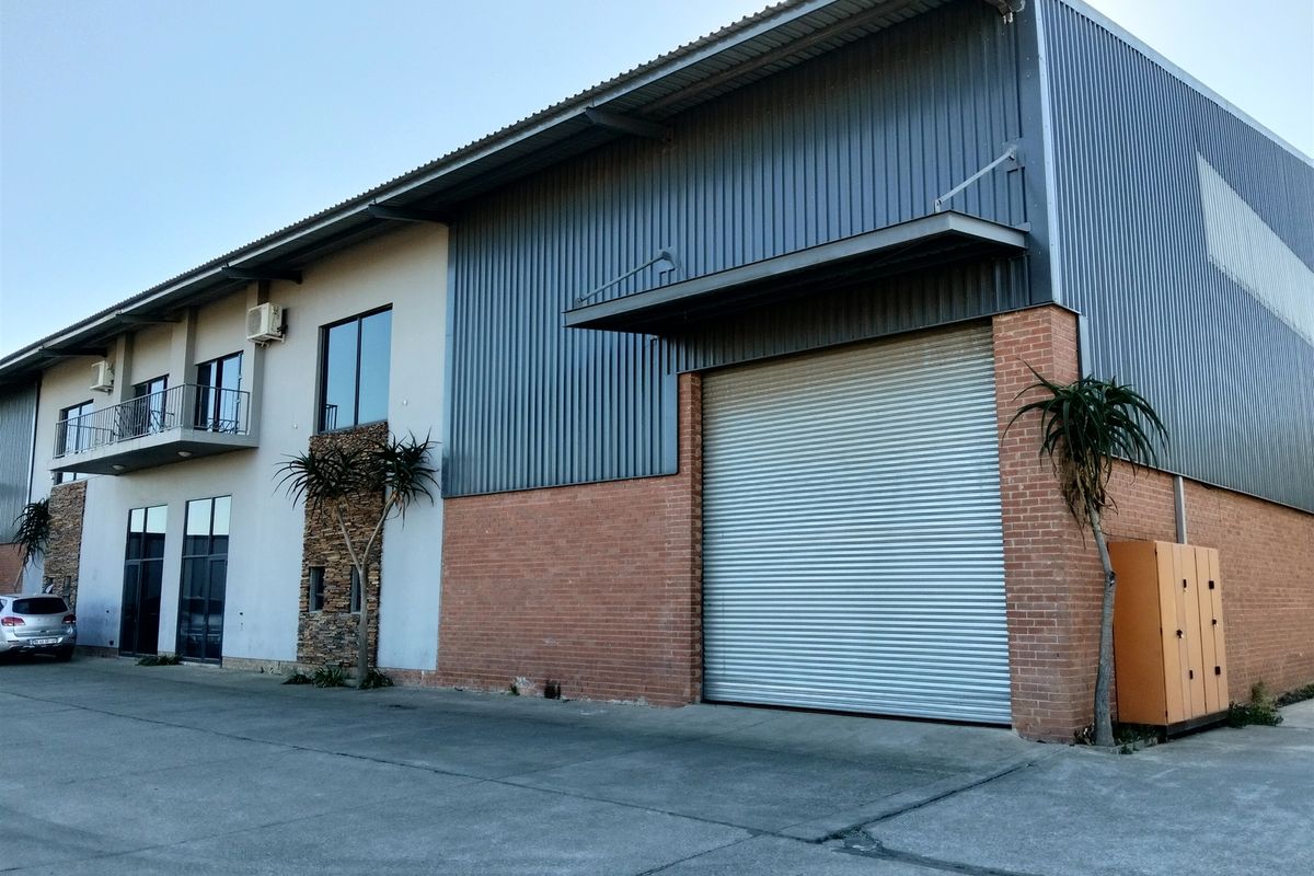 Industrial property featuring a large roller shutter door, metal and brick facade, and an upper-level balcony with concrete driveway access.