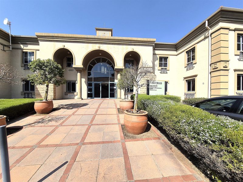 Front exterior view of a professional office building featuring an arched entrance, paved courtyard, and well-maintained landscaping.