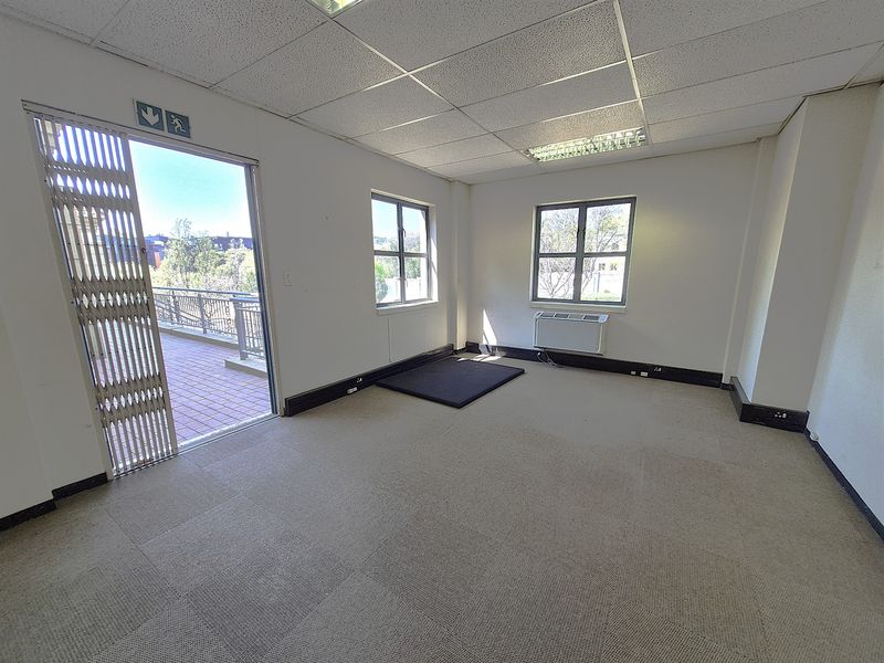 Empty office space featuring carpet tiles, suspended ceiling with recessed lighting, split-unit air conditioning, and direct access to an outdoor balcony area.