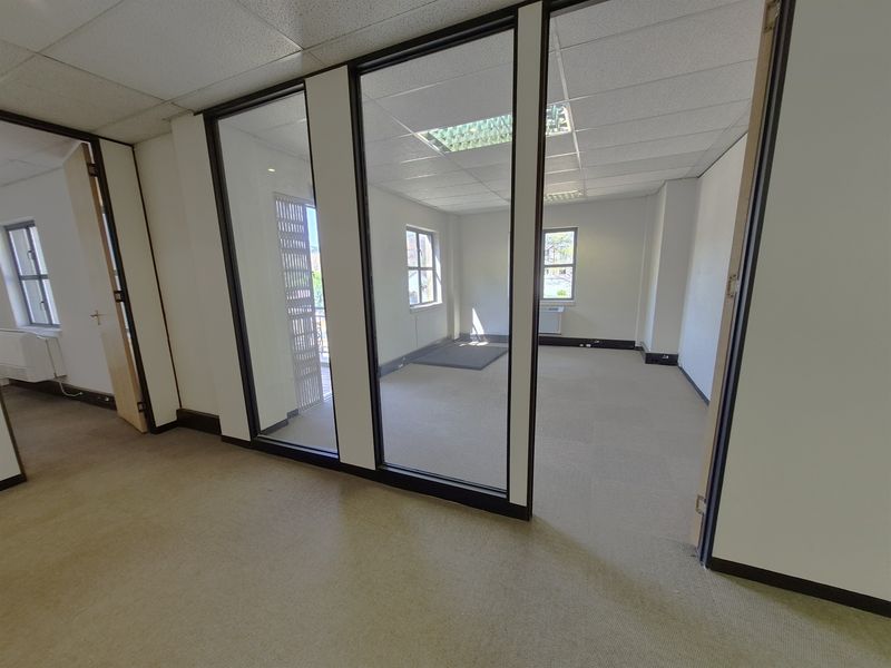 An empty, open-plan office space featuring glass partitions, suspended ceilings, and carpeted flooring, offering a clean and versatile professional work environment.