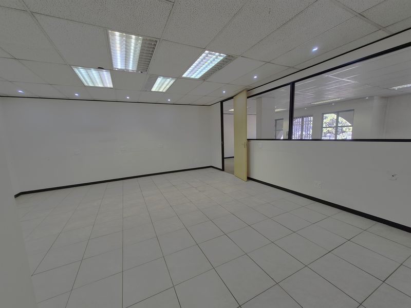 A vacant, open-plan office space featuring tiled flooring, a suspended ceiling with recessed lighting, and a glass partition wall.