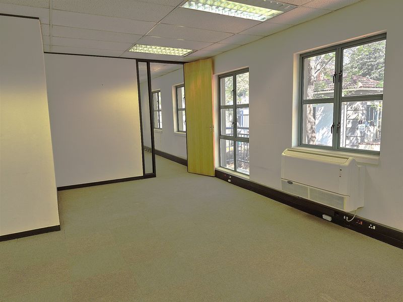 An empty, open-plan office space featuring carpet tiles, suspended ceilings with recessed lighting, and wall-mounted HVAC units.