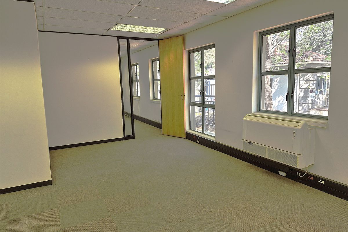 An empty, open-plan office space featuring carpet tiles, suspended ceilings with recessed lighting, and wall-mounted HVAC units.