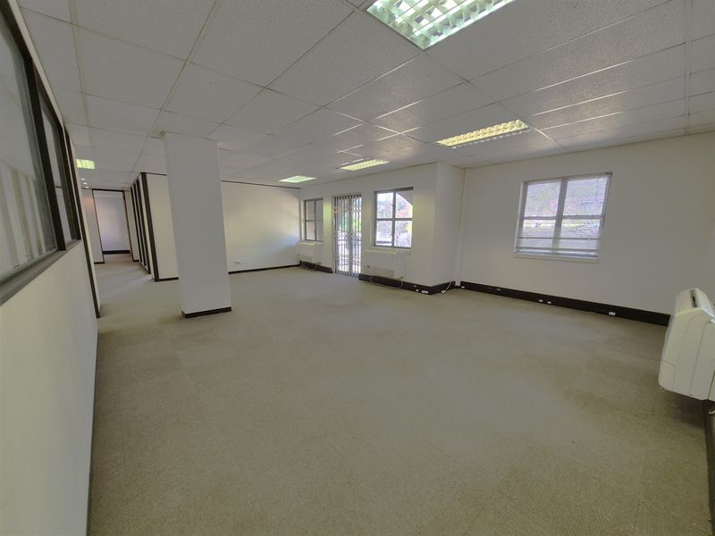 Spacious open-plan office area featuring suspended ceilings, recessed lighting, carpeted flooring, and wall-mounted air conditioning units.