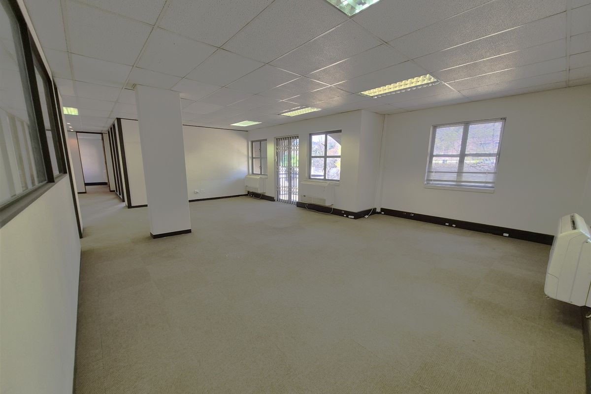 Spacious open-plan office area featuring suspended ceilings, recessed lighting, carpeted flooring, and wall-mounted air conditioning units.