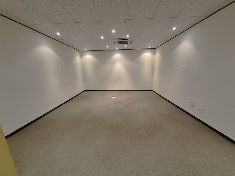 An empty, carpeted office space featuring a suspended ceiling with recessed lighting and integrated air conditioning, ready for custom fit-out.