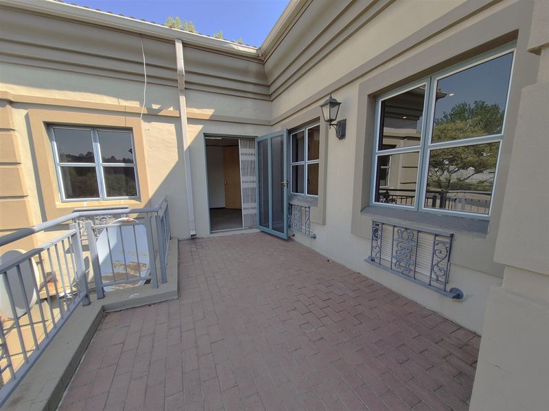 A paved balcony area featuring metal balustrades, security gates, and exterior wall lighting, providing access to the office interior.