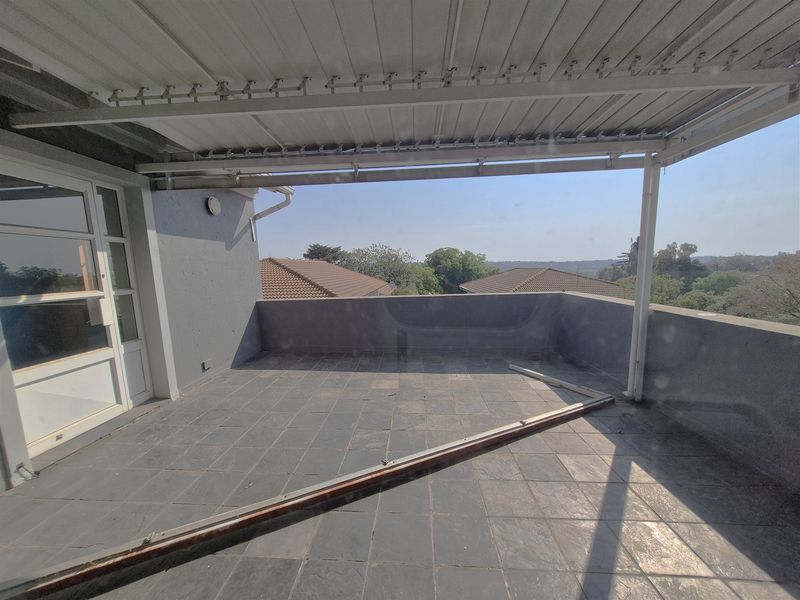 An open-plan balcony featuring tiled flooring, a covered roof structure, and a parapet wall, offering an elevated outdoor space with neighborhood views.