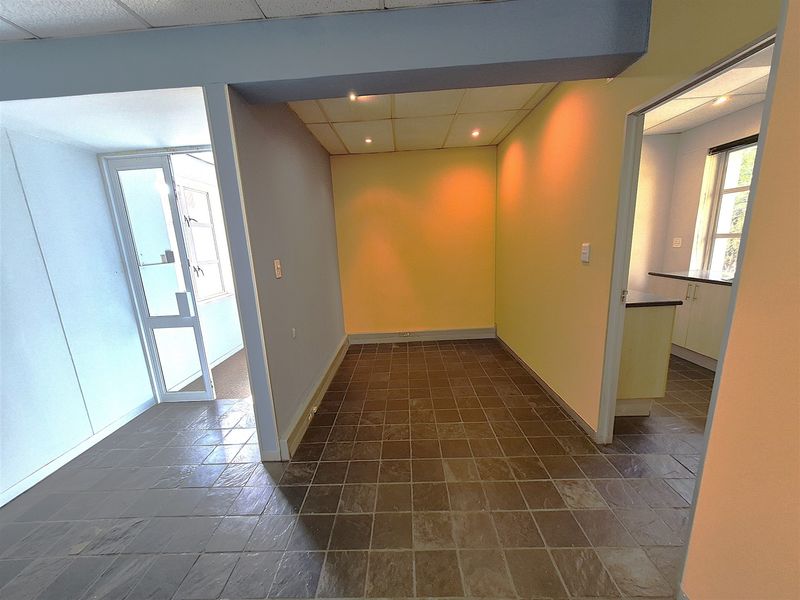 An empty office space featuring tiled flooring, recessed ceiling lighting, and partition walls, offering a functional layout for professional use.