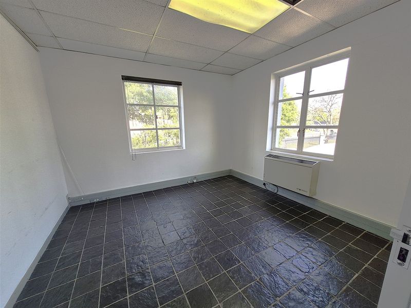 A vacant office space featuring dark tiled flooring, a suspended ceiling with recessed lighting, and an integrated HVAC unit under the windows.