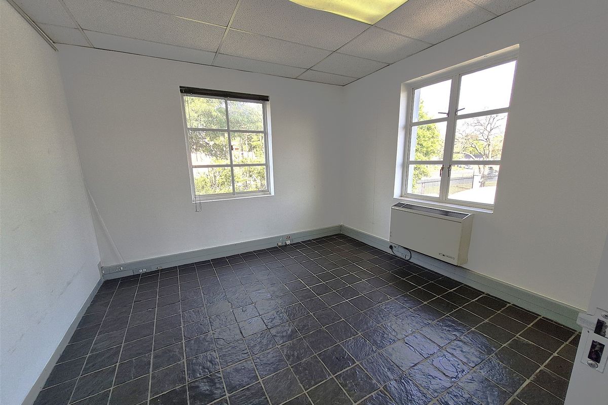A vacant office space featuring dark tiled flooring, a suspended ceiling with recessed lighting, and an integrated HVAC unit under the windows.