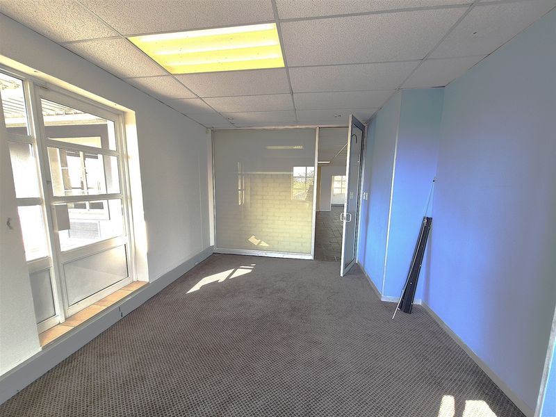 An empty office space featuring a suspended ceiling, recessed lighting, carpeted flooring, and a glass partition wall.