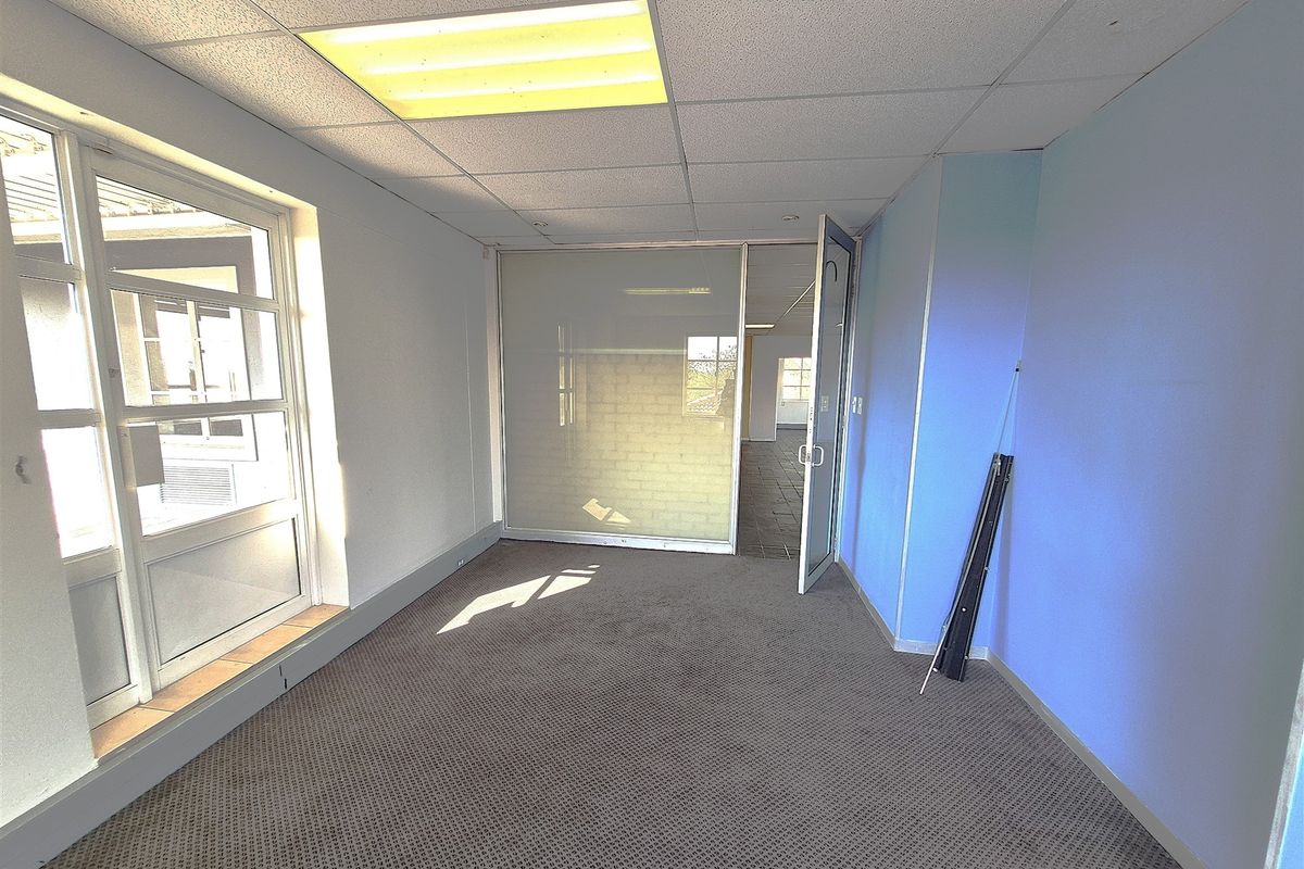 An empty office space featuring a suspended ceiling, recessed lighting, carpeted flooring, and a glass partition wall.
