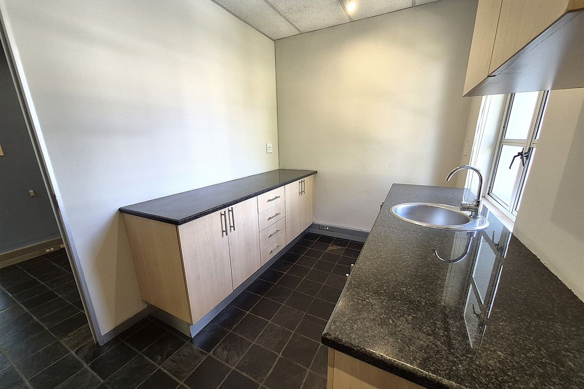 A clean, functional kitchenette featuring light wood cabinetry, dark granite countertops, a stainless steel sink, and durable tiled flooring.