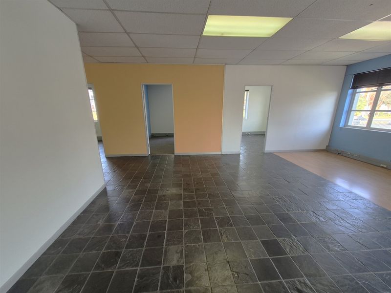 An open-plan office space featuring a mix of slate and laminate flooring, suspended ceilings with recessed lighting, and multiple access points to adjacent rooms.