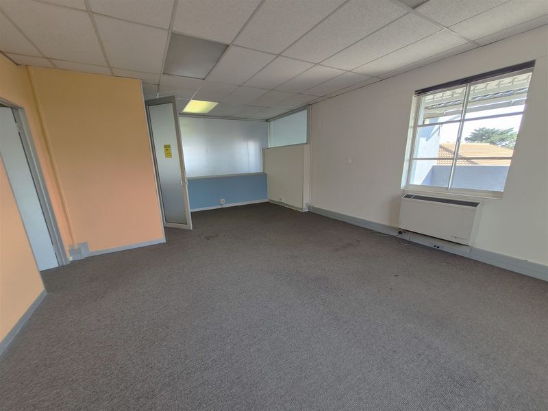 An empty office space featuring a suspended ceiling, carpeted flooring, and an integrated HVAC unit, offering a functional layout for professional use.