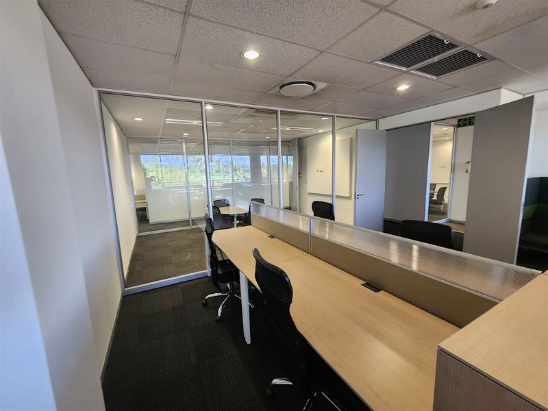 Modern office space featuring glass partitioning, built-in workstations, suspended ceilings with recessed lighting, and carpeted flooring.