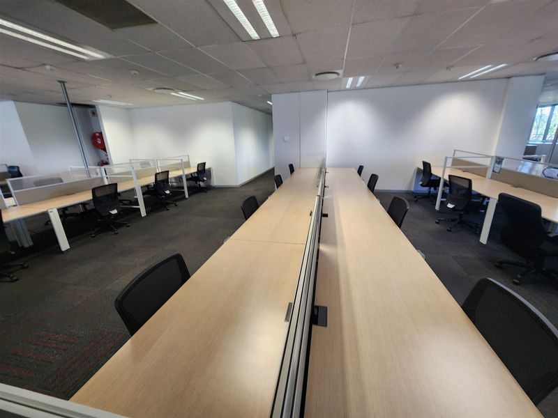 Open-plan office space featuring built-in desk workstations, suspended ceiling with recessed lighting, and carpeted flooring.