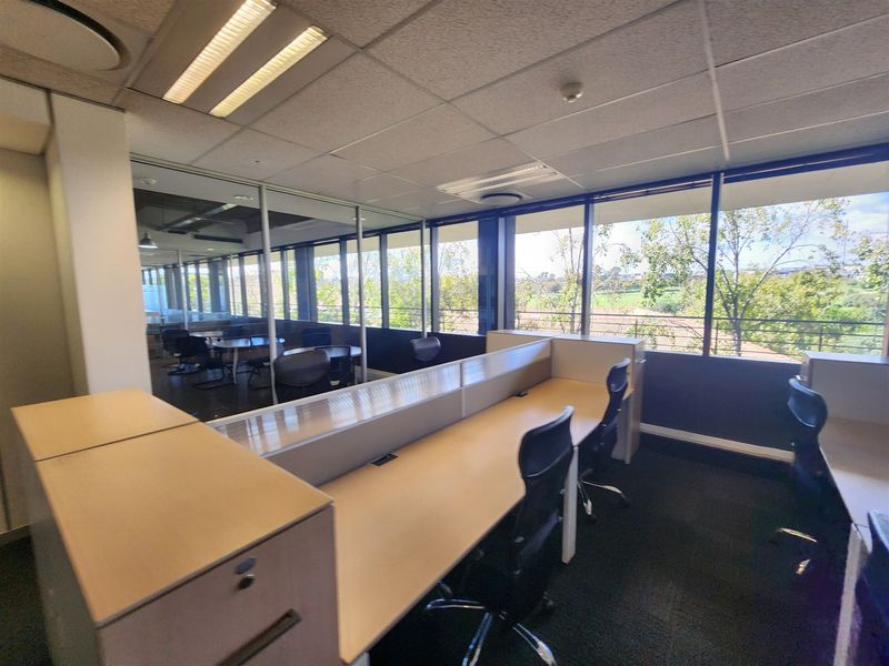 A professional office space featuring built-in desk partitions, large windows with natural light, glass partitioning, and a suspended ceiling with recessed lighting.