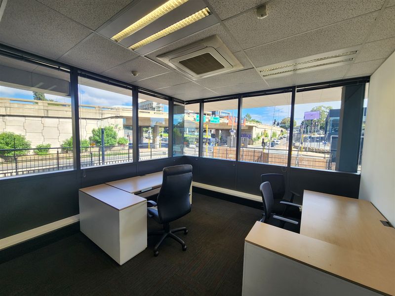 A bright corner office space featuring large windows with urban views, suspended ceilings, integrated air conditioning, and carpeted flooring.