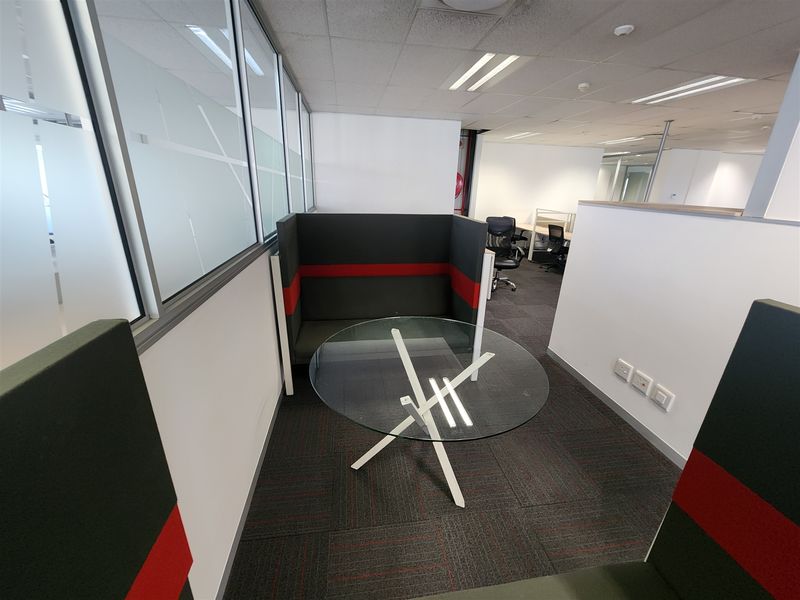 A modern office breakout area featuring glass partitions, carpeted flooring, and recessed ceiling lighting, providing a professional and functional workspace environment.