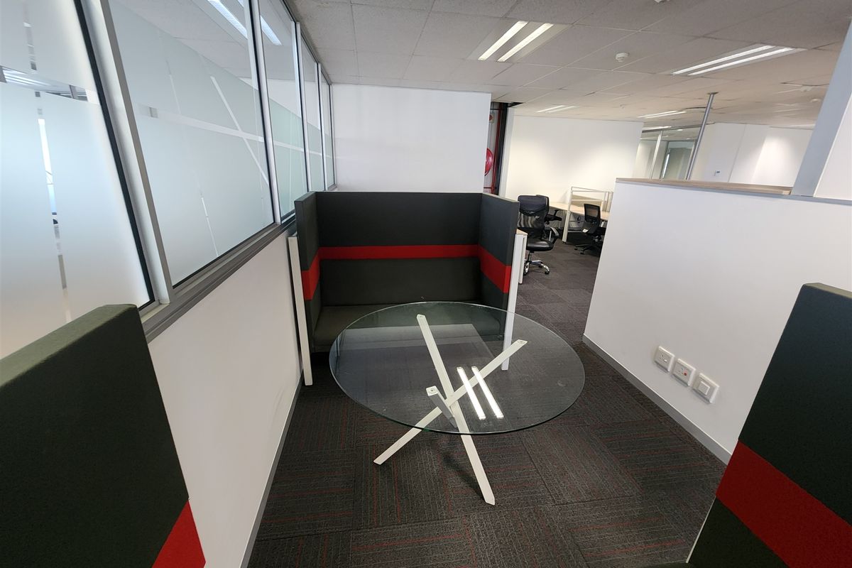 A modern office breakout area featuring glass partitions, carpeted flooring, and recessed ceiling lighting, providing a professional and functional workspace environment.