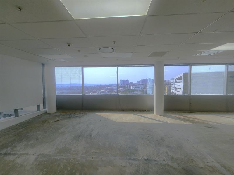 An empty, open-plan office space featuring large windows with city views, suspended ceilings, and unfinished concrete flooring, ready for custom fit-out.