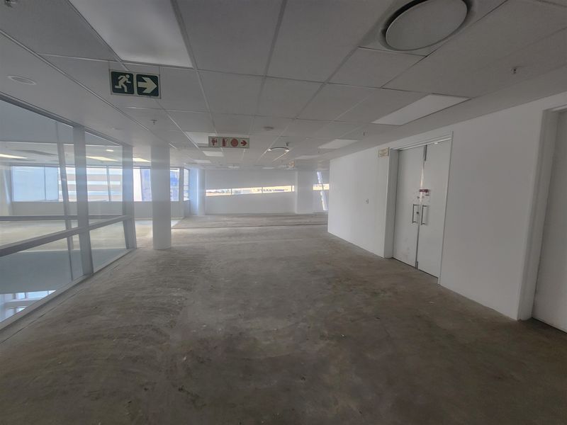 An open-plan office space featuring a suspended ceiling, glass partitioning, and double doors, currently awaiting final flooring installation.