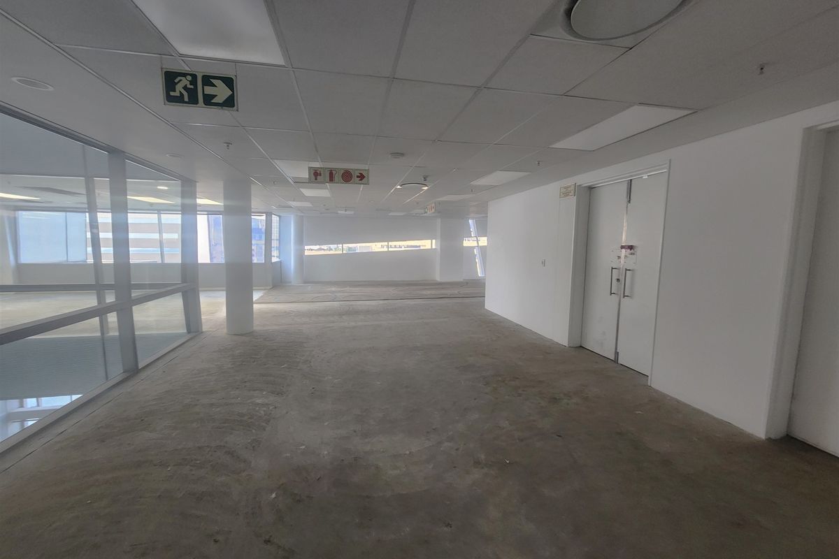 An open-plan office space featuring a suspended ceiling, glass partitioning, and double doors, currently awaiting final flooring installation.
