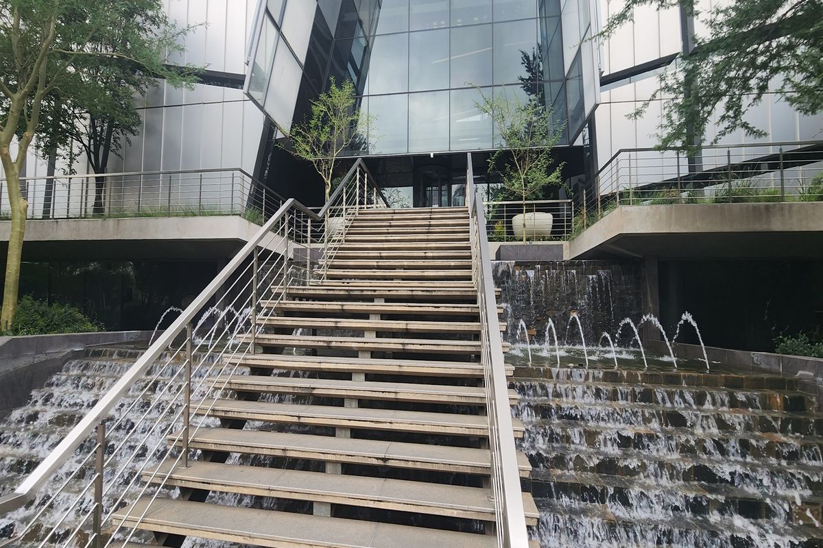 Modern office building entrance featuring a striking glass facade, tiered water feature, and a prominent central staircase with stainless steel railings.