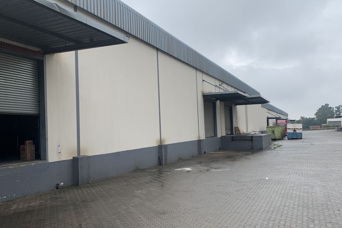 Industrial warehouse exterior featuring multiple loading docks, roller shutter doors, and a spacious paved yard area for logistics and transport access.