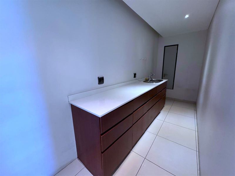 A clean, modern scullery or kitchenette area featuring dark wood cabinetry, a white stone countertop, and an integrated sink.
