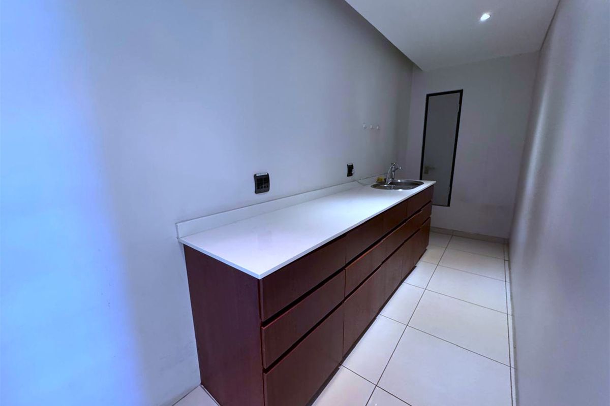 A clean, modern scullery or kitchenette area featuring dark wood cabinetry, a white stone countertop, and an integrated sink.