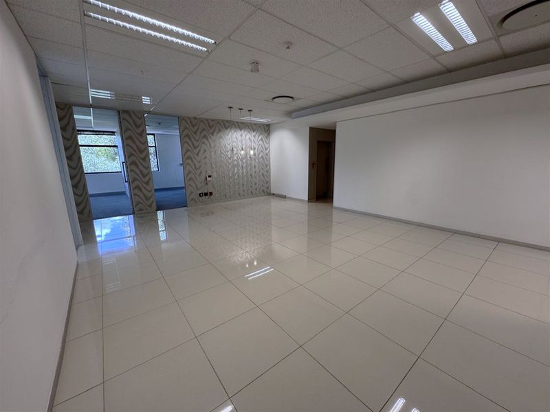 A spacious, vacant office area featuring polished porcelain tile flooring, a suspended ceiling with recessed lighting, and a modern patterned feature wall.