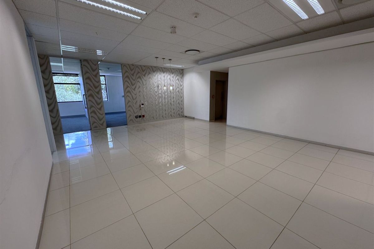 A spacious, vacant office area featuring polished porcelain tile flooring, a suspended ceiling with recessed lighting, and a modern patterned feature wall.