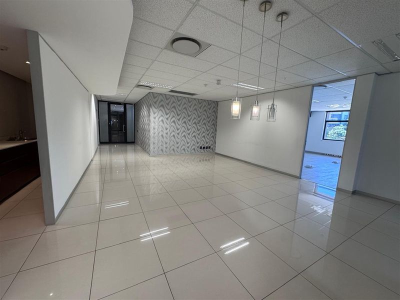A bright, open-plan office space featuring polished porcelain floor tiles, a suspended ceiling with recessed lighting, and a modern glass partition.