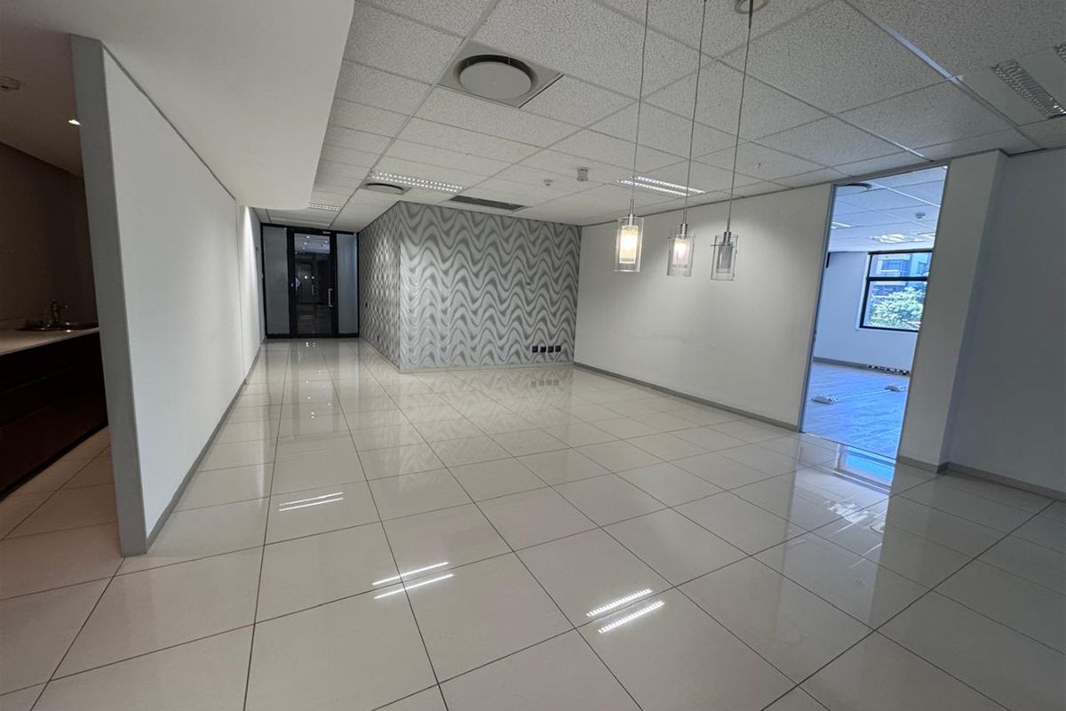 A bright, open-plan office space featuring polished porcelain floor tiles, a suspended ceiling with recessed lighting, and a modern glass partition.