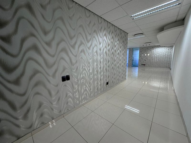 A modern, empty office hallway featuring polished porcelain floor tiles, a suspended ceiling with recessed lighting, and a distinctive patterned feature wall.