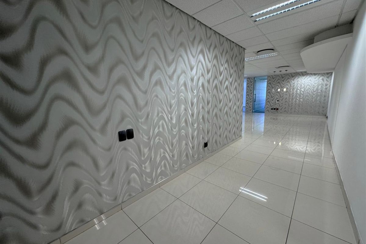 A modern, empty office hallway featuring polished porcelain floor tiles, a suspended ceiling with recessed lighting, and a distinctive patterned feature wall.