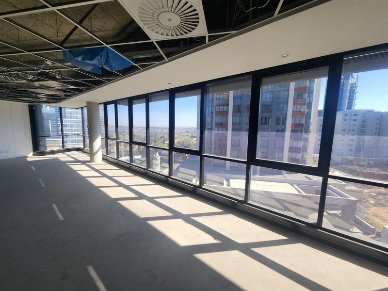An open-plan office space featuring floor-to-ceiling windows with city views, concrete flooring, and an unfinished ceiling grid.