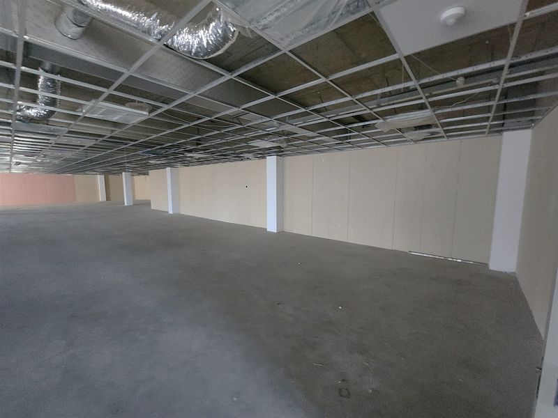 A large, open-plan office space in shell condition, featuring exposed ceiling grid, HVAC ducting, concrete floors, and unfinished drywall partitions.