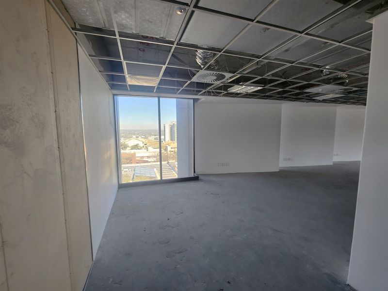 An unfinished open-plan office space featuring a suspended ceiling grid, exposed HVAC components, and large windows with city views.