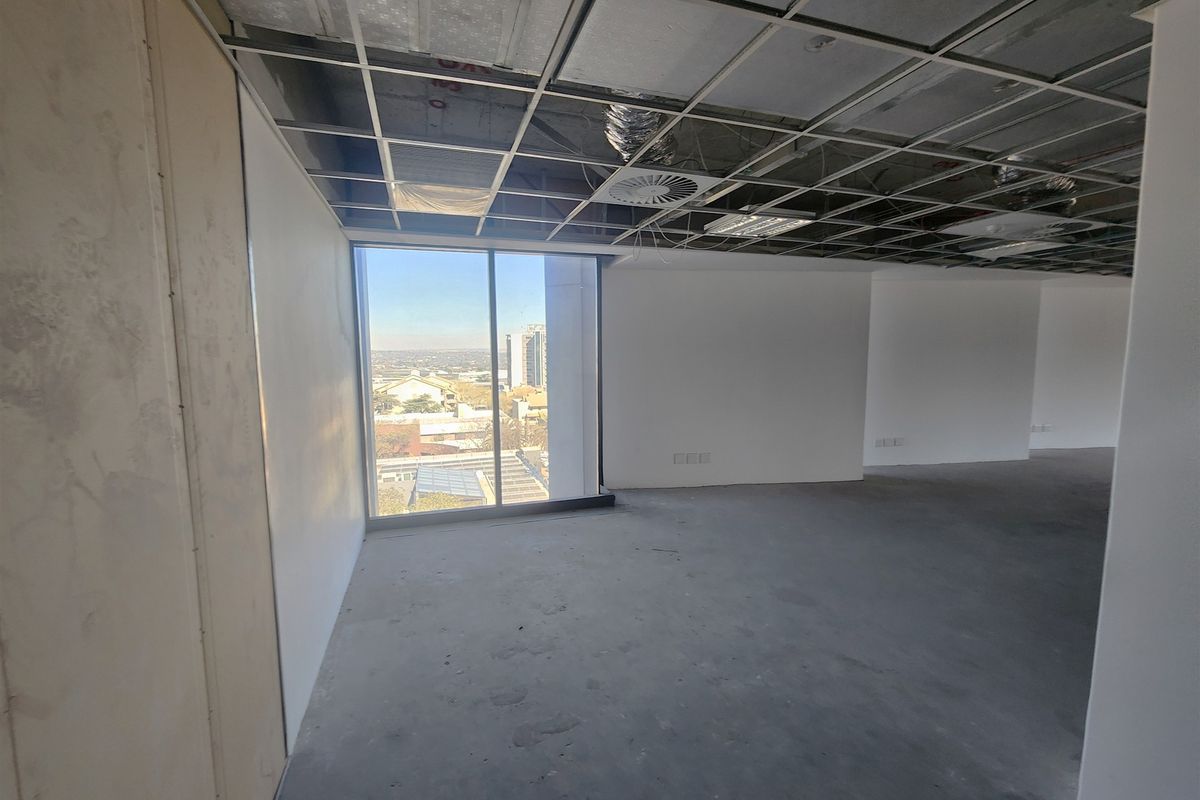 An unfinished open-plan office space featuring a suspended ceiling grid, exposed HVAC components, and large windows with city views.