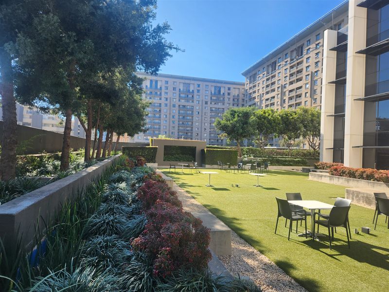A well-maintained outdoor garden area featuring artificial turf, landscaped garden beds, and retaining walls, providing a pleasant communal space for the office complex.