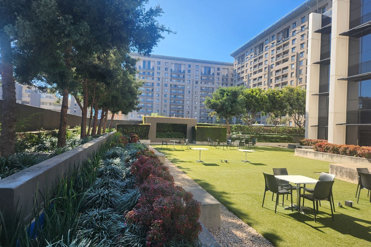 A well-maintained outdoor garden area featuring artificial turf, landscaped garden beds, and retaining walls, providing a pleasant communal space for the office complex.